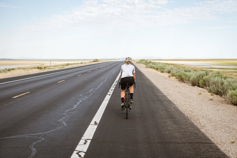 Una mujer en bicicleta por una carretera desierta.