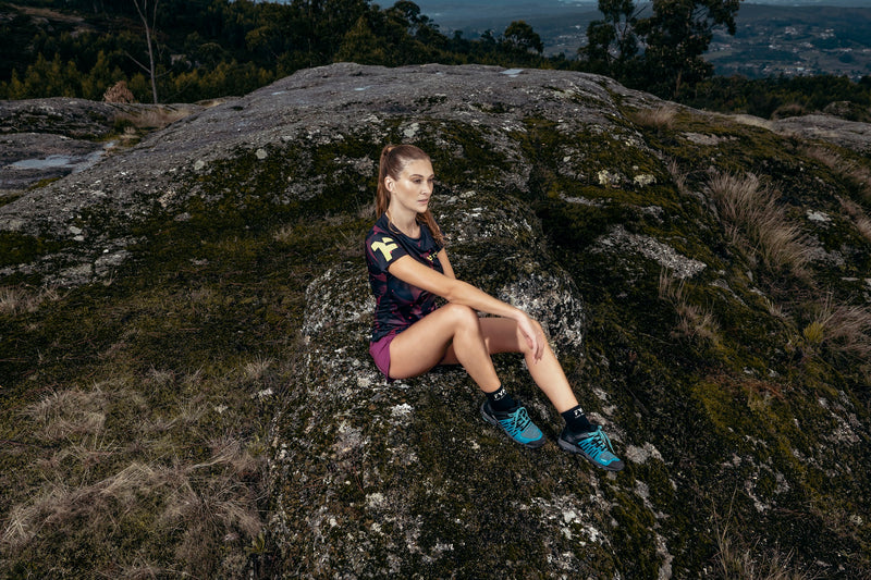 Uma mulher com roupa de corrida sentada numa rocha.