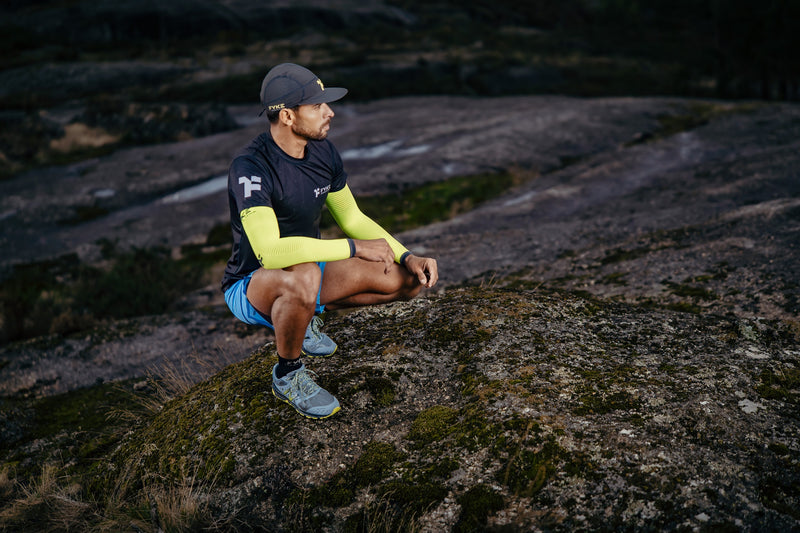 Um homem com chapéu e roupa de trail running Fyke aninhado num terreno rochoso.