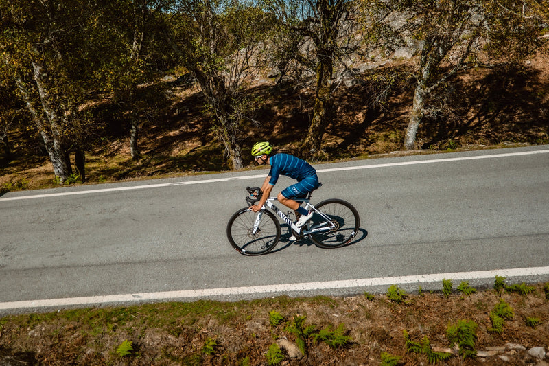 Ciclista com equipamento da marinha e capacete amarelo fluorescente a descer uma estrada no meio da floresta